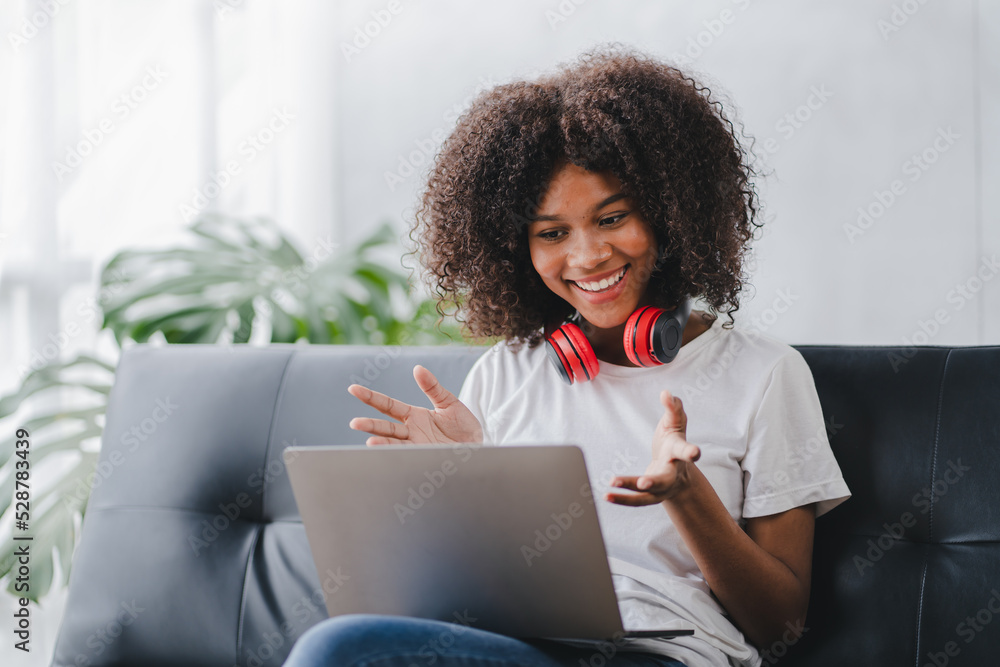 african american woman sitting on sofa at home video call chatting with friends using a laptop and a smartphone or phone african american woman sitting on sofa at home video call chatting with friends using a laptop and a smartphone or phone