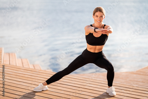 Sporty middle aged female in activewear making side lunges exercise outdoors