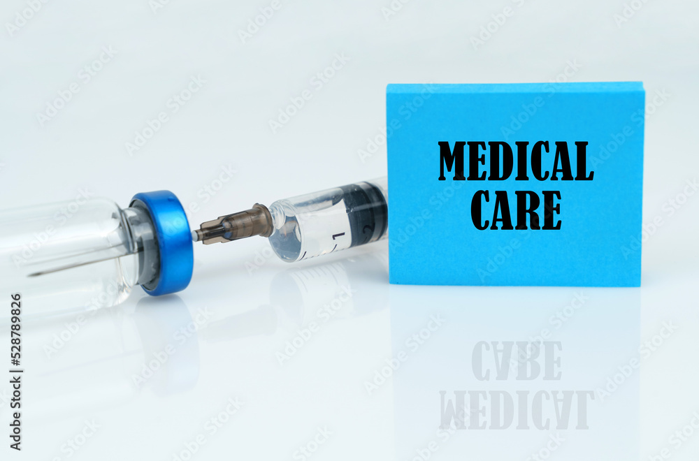 On a white reflective surface there is a syringe with an ampoule and a plate with the inscription - MEDICAL CARE On a white reflective surface there is a syringe with an ampoule and a plate with the inscription - MEDICAL CARE