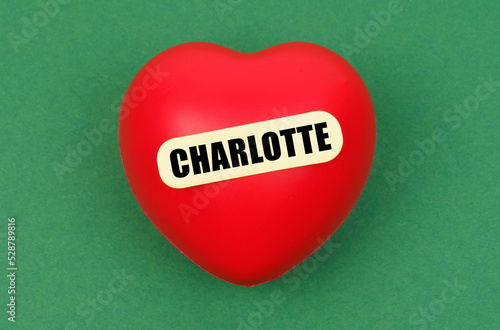 On a green surface lies a red heart with the inscription - Charlotte