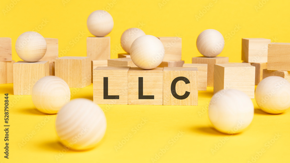 text LLC is written on wooden cubes. bright yellow surface. business concept. wooden sphere balls among the wood cubes, different and position in niche market concept text LLC is written on wooden cubes. bright yellow surface. business concept. wooden sphere balls among the wood cubes, different and position in niche market concept