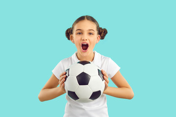 Funny girl child isolated on blue studio background hold ball cheer support sport team. Happy excited teen kid scream and yell for favorite football team goal score. Children hobby concept.