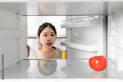 Upset chinese woman looking at lonely tomato in her fridge