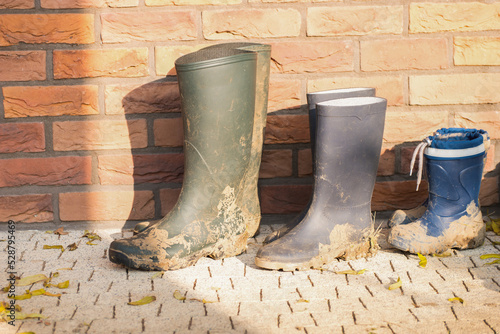 Three dirty boots of all family members. Boots of child and parents. In the fall there is a lot of work in the garden. Children help with gardening. Lot of mud on the boots. photo