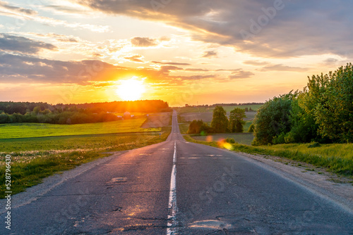 Beautiful sunset over an empty road in the countryside. An empty asphalt road runs along a field and forest during sunset.