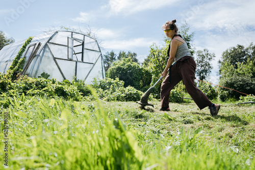 Wallpaper Mural Woman cutting grass with a trimmer and a greenhouse in. the background Torontodigital.ca