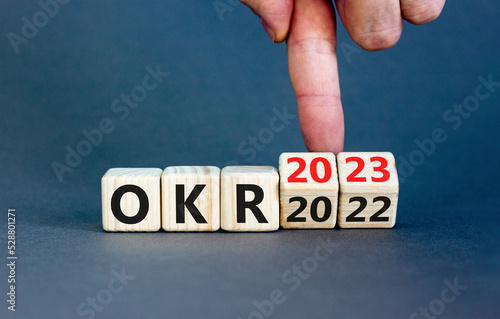 OKR, objectives and key results symbol. Businessman turns cubes with words OKR 2022 and OKR 2023 on beautiful grey background. Business OKR 2023 objectives and key results concept. Copy space.