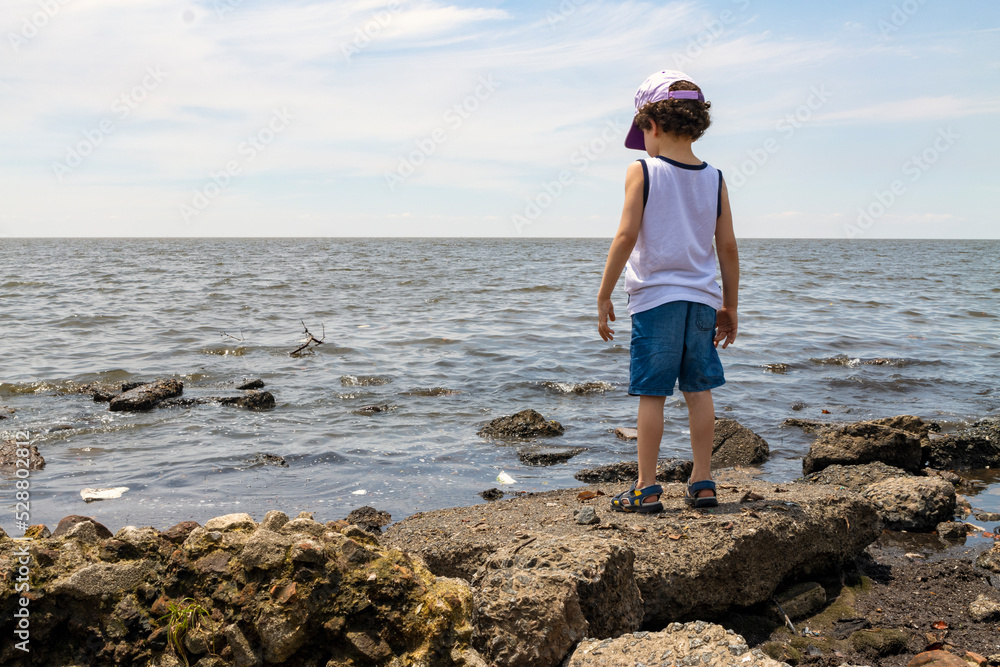 child looking at polluted river from the shore, environmental concept