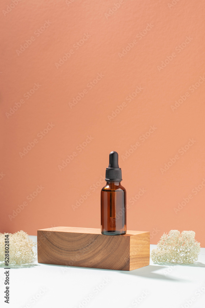 Bottle with pipette made of dark glass, cosmetic product woodenpedestal. Pastel coral background