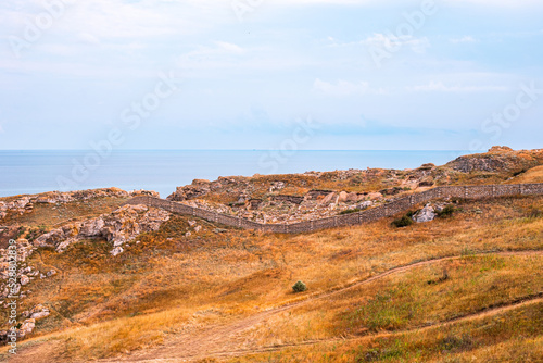 Sea coast with mountains with dry grass  along which a long stone fence stretches. Travel and tourism