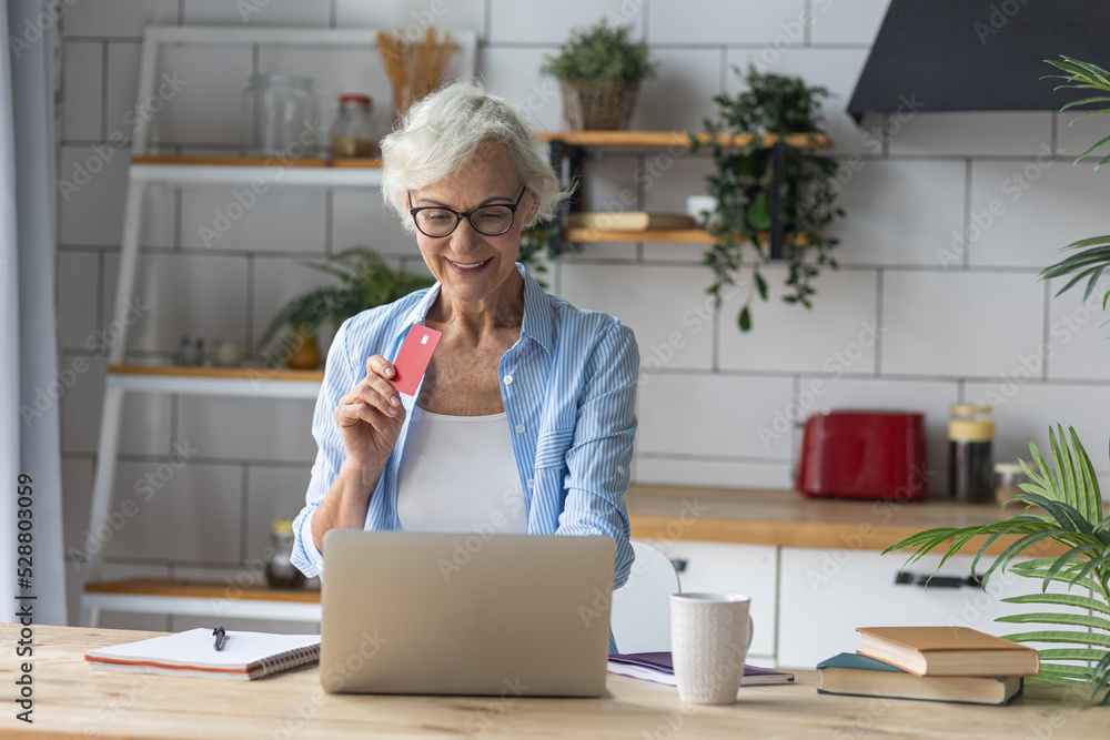 Beautiful senior woman with short grey hair and lovely smile shopping in the internet at home with a credit card. Concept of mature woman using technology Beautiful senior woman with short grey hair and lovely smile shopping in the internet at home with a credit card. Concept of mature woman using technology