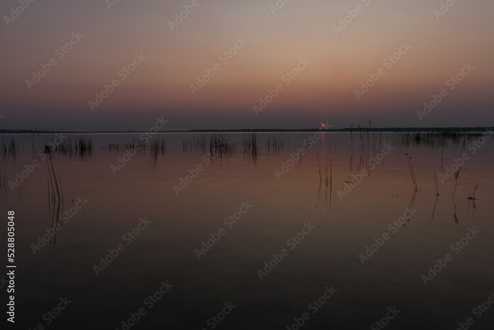 Sunset on the lake. Evening sky with beautiful solar disk is reflected in the water of the lake