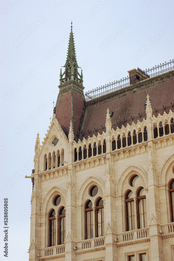 Buildings in the Parliament House of Budapest, Hungary, are popular destination sites. Photo shows steep red roof line with embellished points and window with arches and round windows above.. 