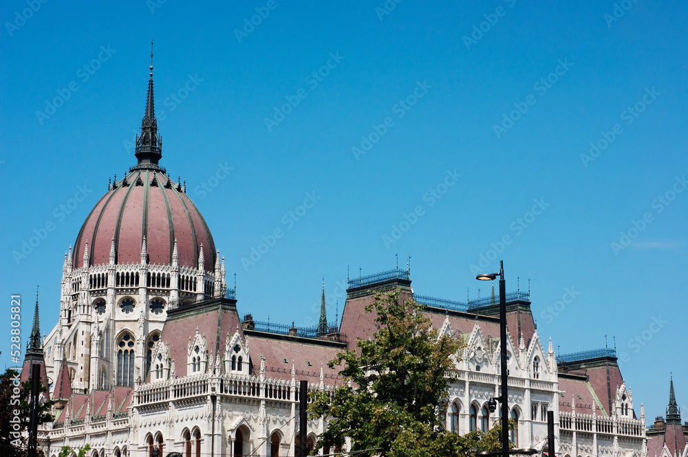 Obraz premium The red roof dome of the Parliament House in Budapest, Hungary, is only a small part of the massive government buildings with awesome spires, arches, towers, and railings.