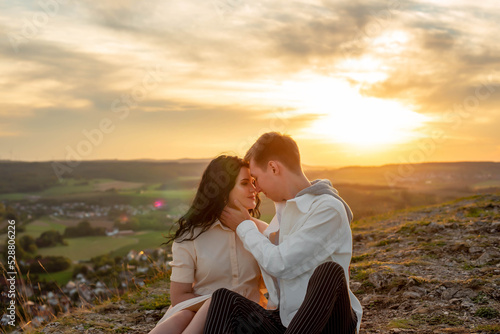 A couple in love, a guy and a girl are sitting on a mountain at sunset kissing and hugging