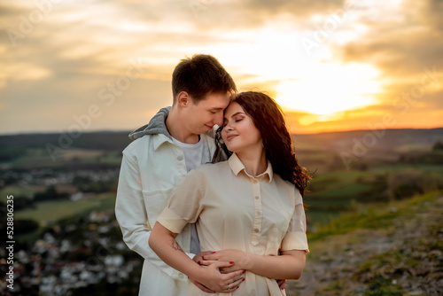 A couple in love, a guy and a girl are standing on a mountain at sunset hugging and kissing