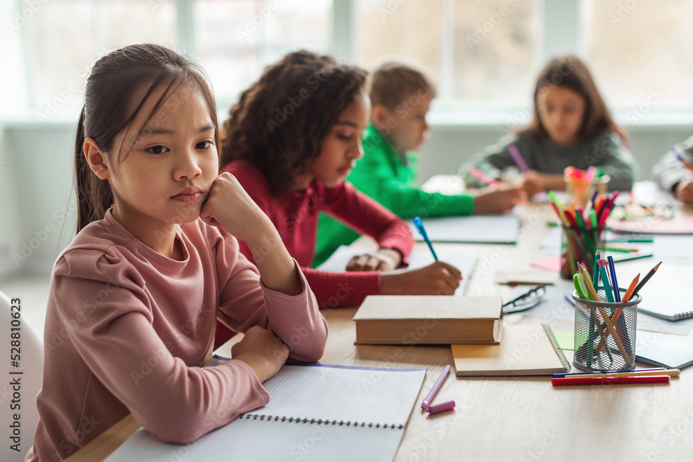 Unhappy Asian Schoolgirl Thinking Sitting With Diverse Classmates In Classroom Unhappy Asian Schoolgirl Thinking Sitting With Diverse Classmates In Classroom