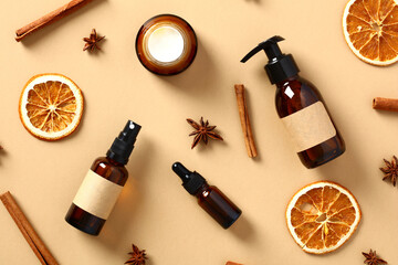 Amber glass cosmetics bottles with dried orange slices, cinnamon sticks, anise stars on beige table. Autumn fall beauty products set.