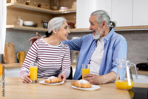 Portrait Of Happy Senior Spouses Having Snacks In Kitchen Together