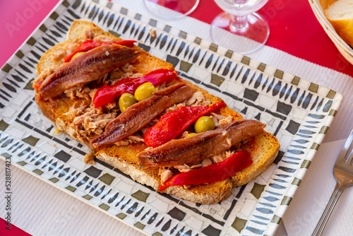 Delicious toasts with shredded canned tuna, anchovies, roasted bell pepper slices and olives. Mediterranean appetizer