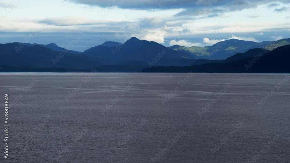Beautiful sun-dappled mountains line the Inside Passage route into Juneau, Alaska under a dynamic cloudy sky along peaceful waters