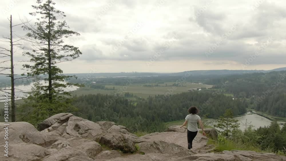 Adventurous Woman Standing on top of a rock overlooking the Canadian Nature Landscape. Minnekhada Regional Park, Coquitlam, Vancouver, British Columbia, Canada. Adventurous Woman Standing on top of a rock overlooking the Canadian Nature Landscape. Minnekhada Regional Park, Coquitlam, Vancouver, British Columbia, Canada.