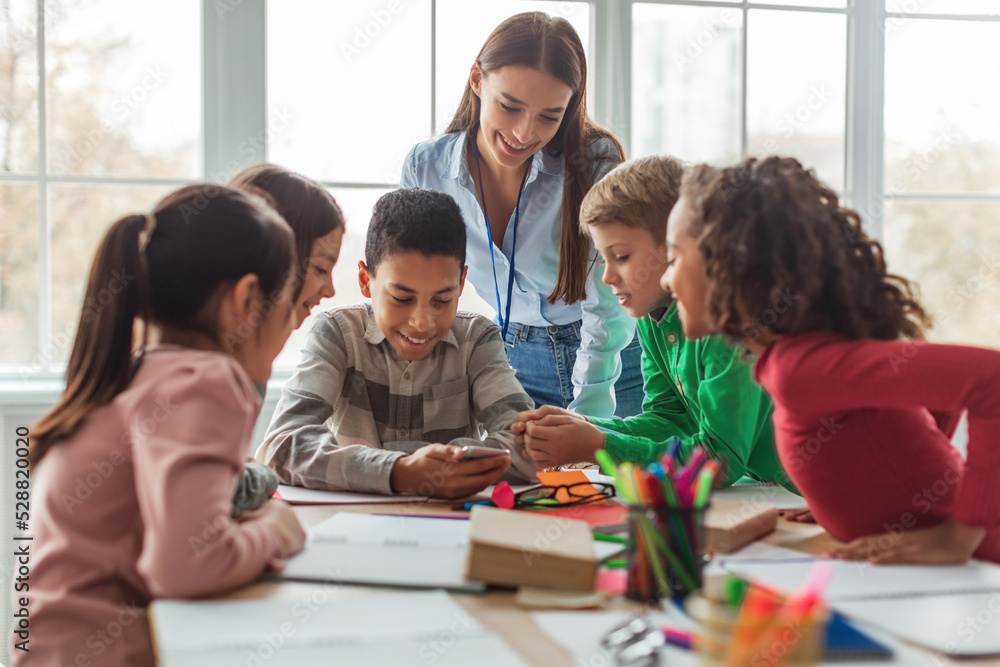 Multiethnic School Kids And Teacher Using Smartphone In Modern Classroom Multiethnic School Kids And Teacher Using Smartphone In Modern Classroom