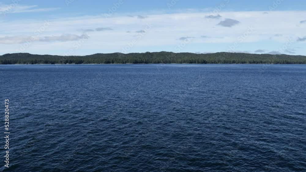 Dark calm blue waters of the Alaska Inside Passage accent the forested pine-tree lined shores in the distance Dark calm blue waters of the Alaska Inside Passage accent the forested pine-tree lined shores in the distance