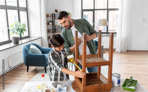 family, diy and home improvement concept - father and son with ruler measuring old round wooden table for renovation at home