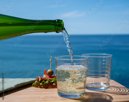 Pouring of txakoli or chacolí slightly sparkling very dry white wine produced in the Spanish Basque Country, served outdoor with view on Bay of Biscay, Atlantic Ocean. photo