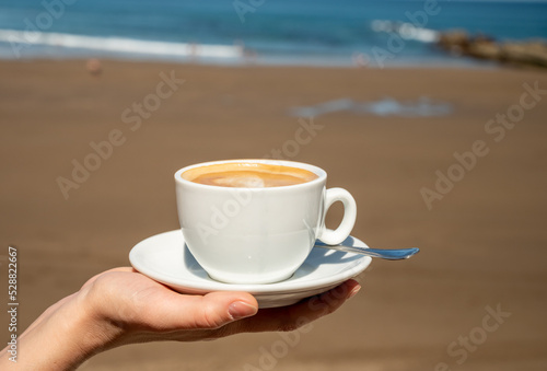 Drinking cappuccino coffee on Atlantic ocean with view on sandy beach