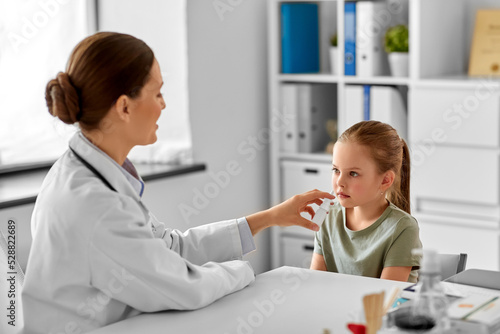 medicine, healthcare and pediatry concept - female doctor or pediatrician and little girl patient blowing her nose on medical exam at clinic