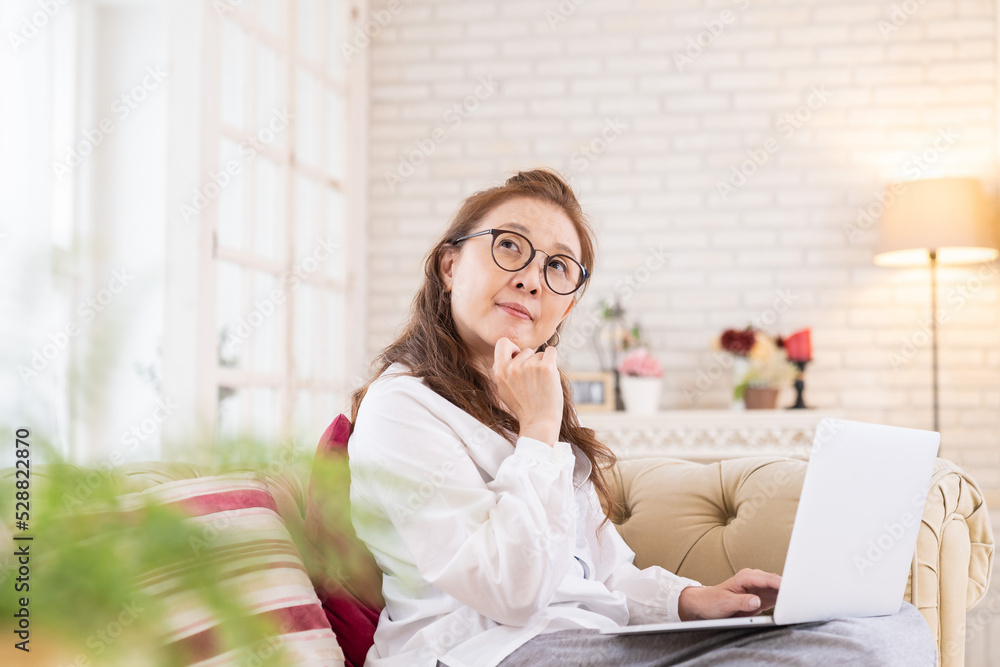 部屋でラップトップコンピューターを見るシニア女性 考える 部屋でラップトップコンピューターを見るシニア女性 考える