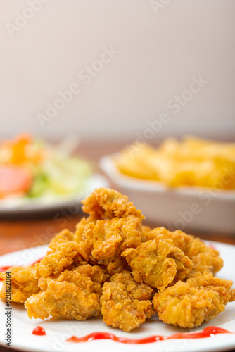 Chicken chicharron, accompanied by French fries and salad on a wooden table.