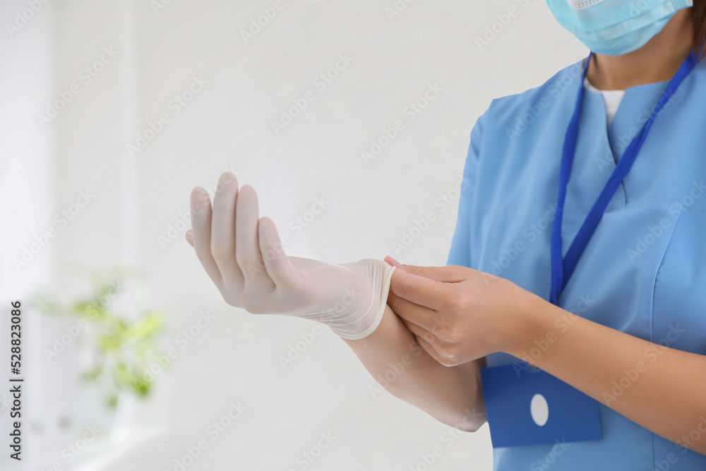 Doctor putting on medical gloves against blurred background, closeup Doctor putting on medical gloves against blurred background, closeup