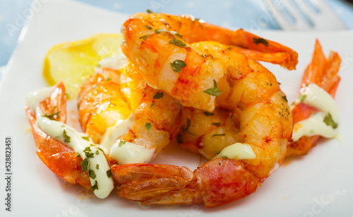 Grilled shrimps served with herbs, garlic sauce and lemon on white plate