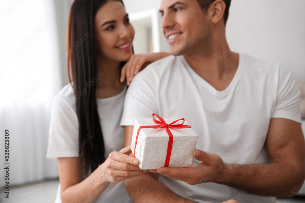 Man presenting gift to his beloved woman at home, focus on box. Valentine's day celebration Man presenting gift to his beloved woman at home, focus on box. Valentine's day celebration