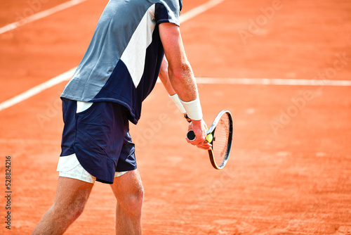 Illustration shows the body of a player (tennisman) about to serve with his racquet and a ball in his hands, playing on a clay tennis court photo