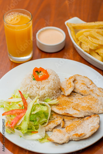 Grilled chicken accompanied by rice with french fries and salad.