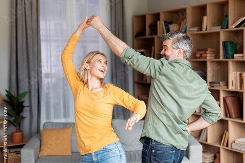Portrait Of Positive Middle Aged Couple Dancing In Living Room Interior