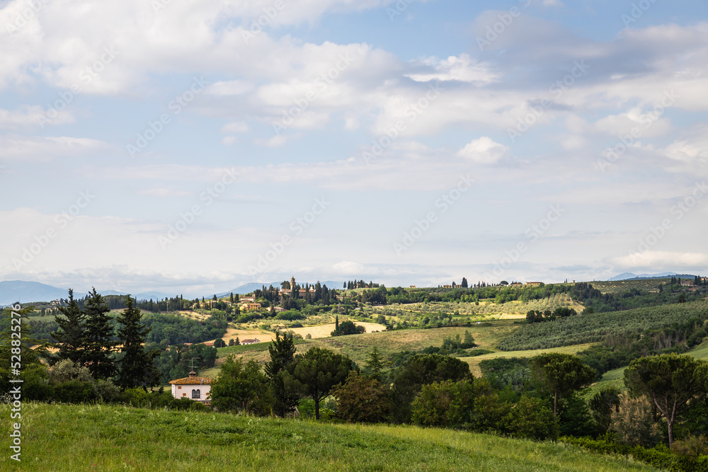 Fototapeta premium Rural view of Tuscany with rolling green hills and traditional Tuscan architecture on a partly sunny day.