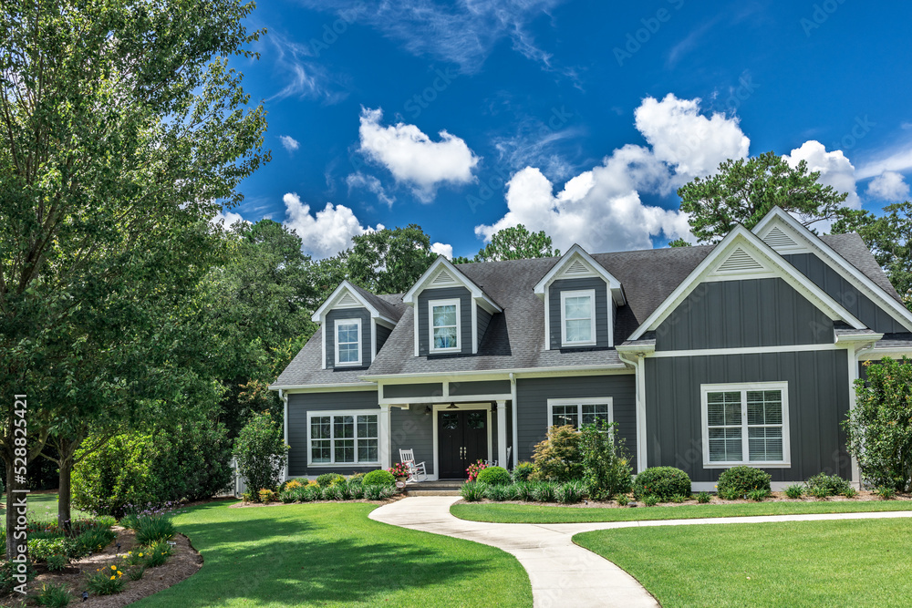 A large gray craftsman new construction house with a landscaped yard and leading pathway sidewalk