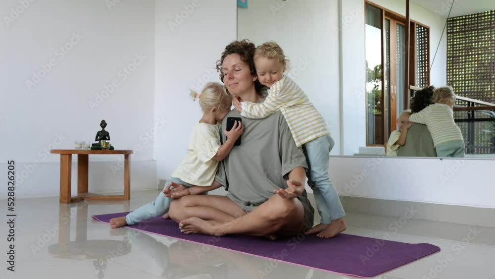 Two girls lovingly hug their mother who is meditating on a mat in the lotus position. The love of children for their spiritually developed mother who practices meditation to calm her nerves. Two girls lovingly hug their mother who is meditating on a mat in the lotus position. The love of children for their spiritually developed mother who practices meditation to calm her nerves.