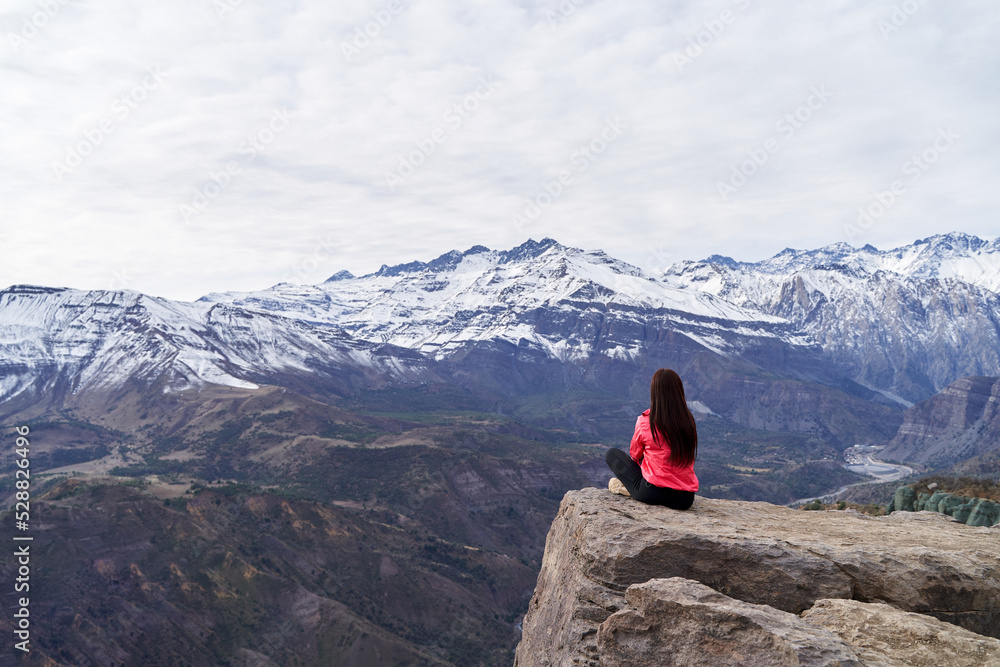 young woman with red jacket on her back contemplating the Andes Mountains of Chile