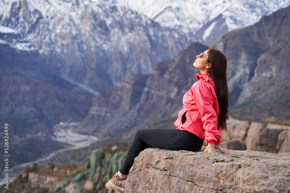 Naklejka premium young woman on her side in red jacket sitting on a rock breathing in the middle of the Andes Mountains of Chile