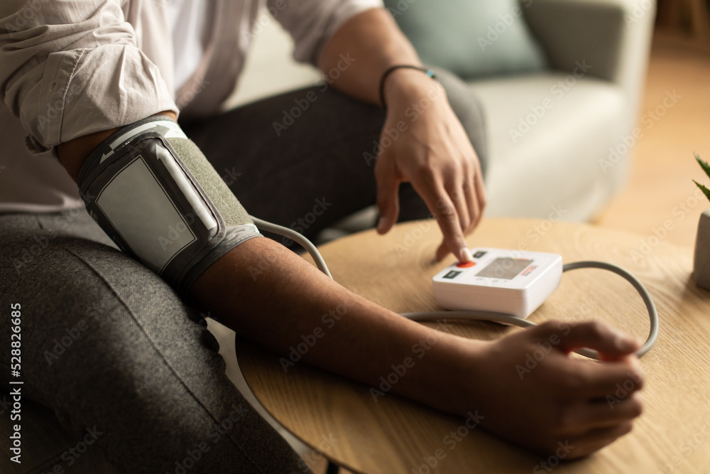 Obraz premium Closeup of young black man checking blood pressure, using modern tonometer at home