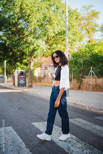 Black teenager holding a coffee cup and wearing sunglasses. She is walking in the city. © Pablo Rasero
