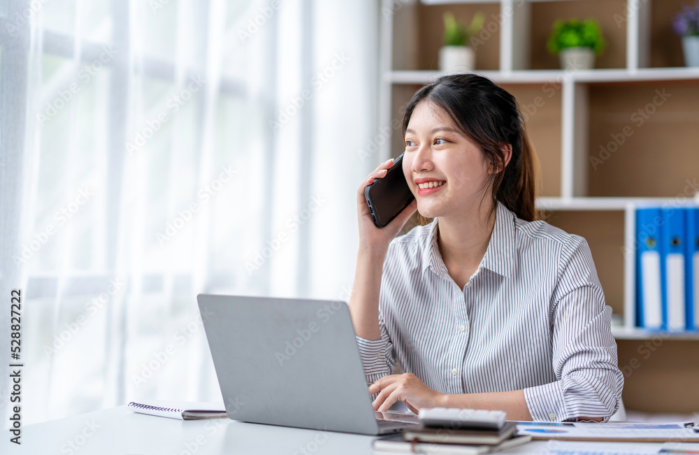 Young woman talking on the phone working on laptop in office. Asian businesswoman sitting in her office in office. Beautiful woman freelancer working online at her home. Young woman talking on the phone working on laptop in office. Asian businesswoman sitting in her office in office. Beautiful woman freelancer working online at her home.