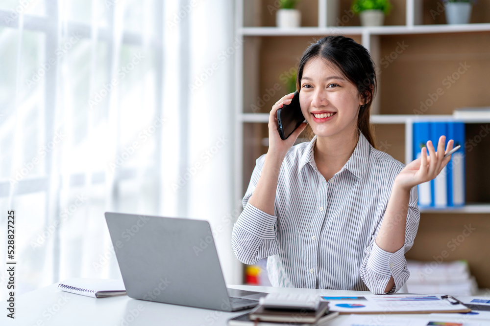 Young woman talking on the phone working on laptop in office. Asian businesswoman sitting in her office in office. Beautiful woman freelancer working online at her home. Young woman talking on the phone working on laptop in office. Asian businesswoman sitting in her office in office. Beautiful woman freelancer working online at her home.