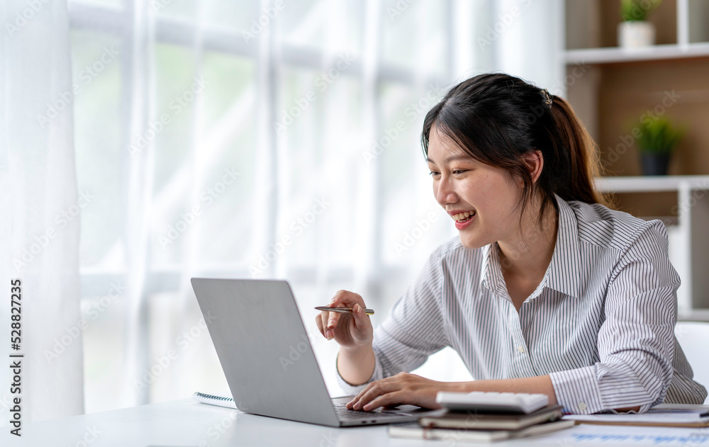 Asian woman freelancer is working her job on a laptop computer in a modern office. Doing accounting analysis report real estate investment data, Financial and tax systems concept. Asian woman freelancer is working her job on a laptop computer in a modern office. Doing accounting analysis report real estate investment data, Financial and tax systems concept.